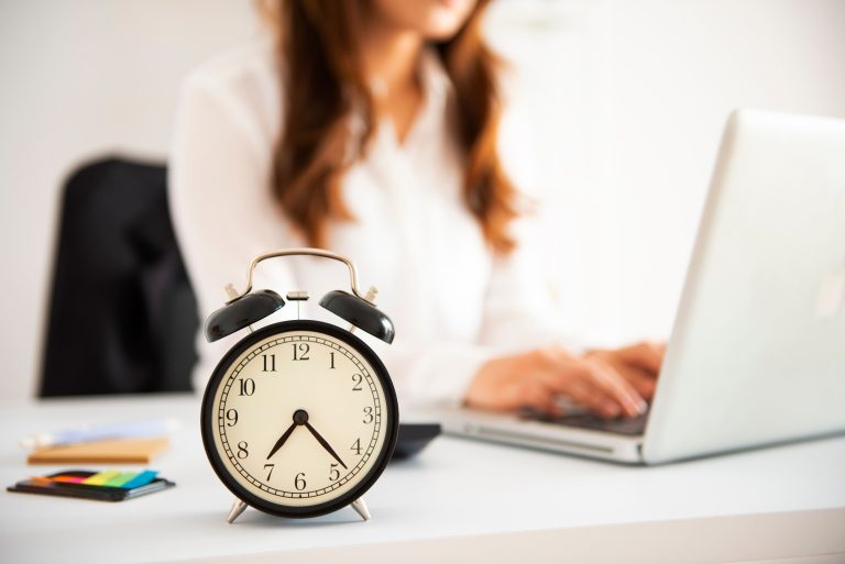 An alarm clock on a desk beside an employee working at a laptop