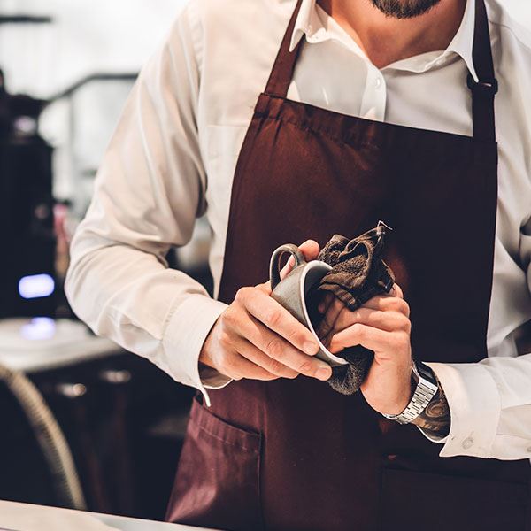 Barista in an apron polishing a cup behind a cafe counter