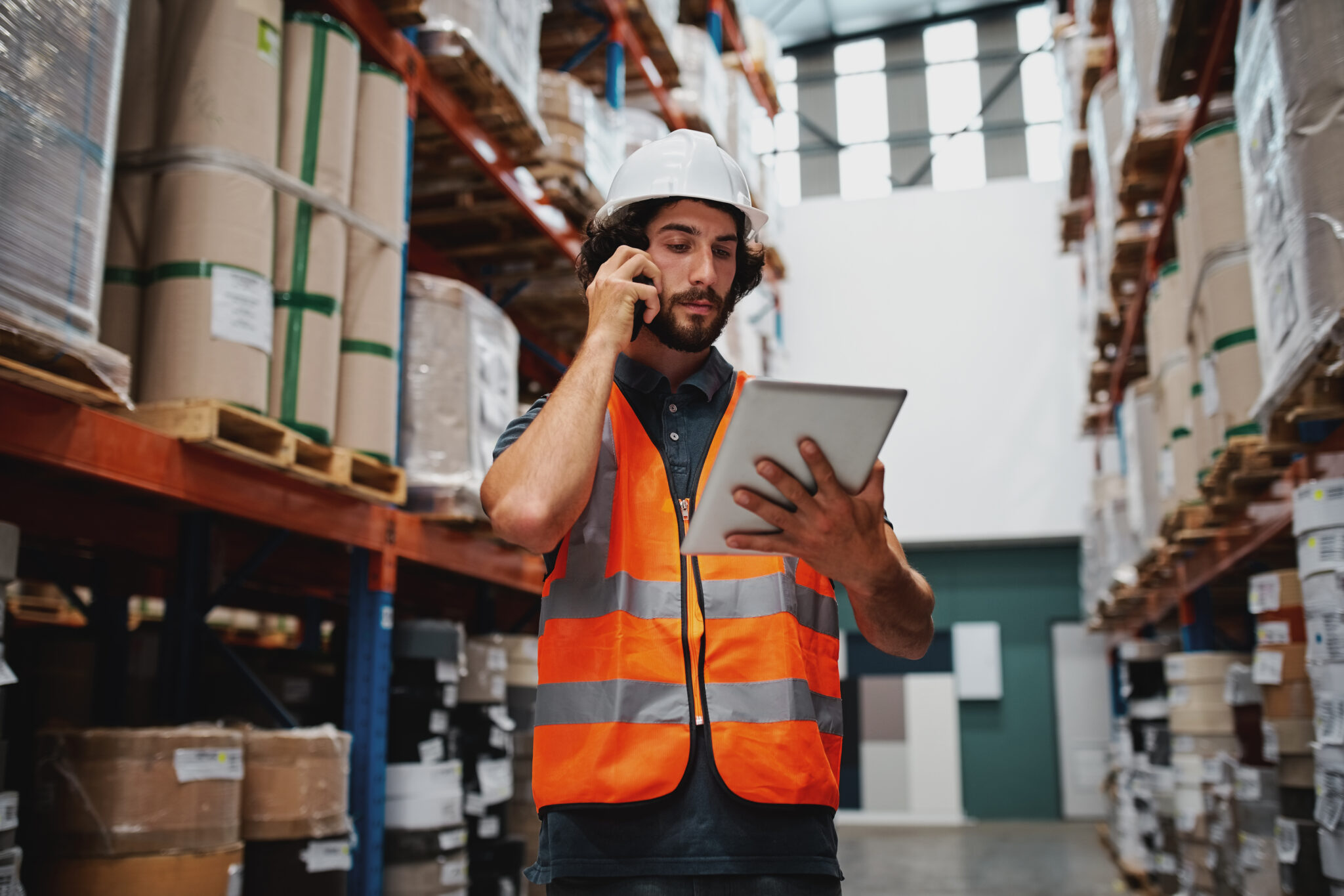 Warehouse worker in a hard hat and safety vest checking a tablet
