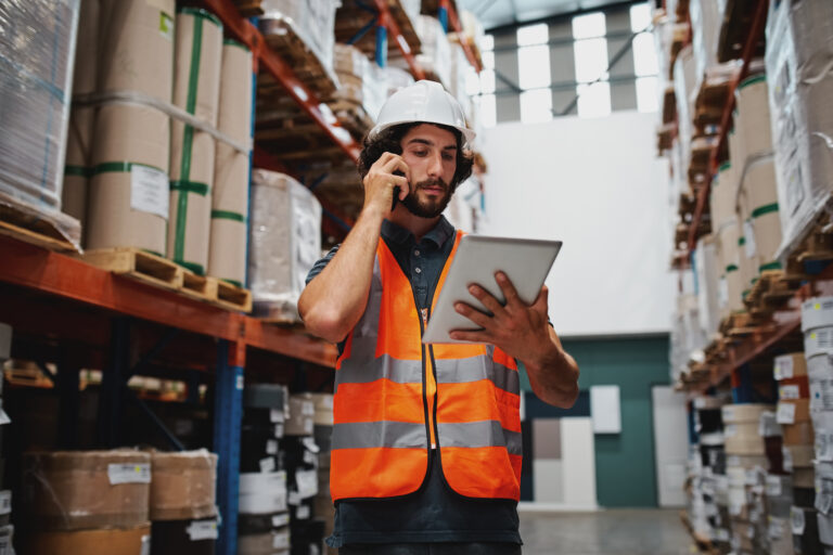 Warehouse worker in a hard hat and safety vest checking a tablet